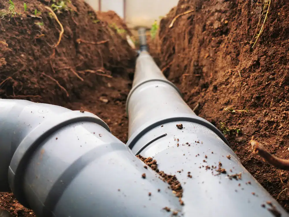 Close-up view of large black plastic pipes laid in a trench with brown soil on both sides, likely part of an underground plumbing or drainage installation project for basement waterproofing in Montgomery & Chester County, PA.